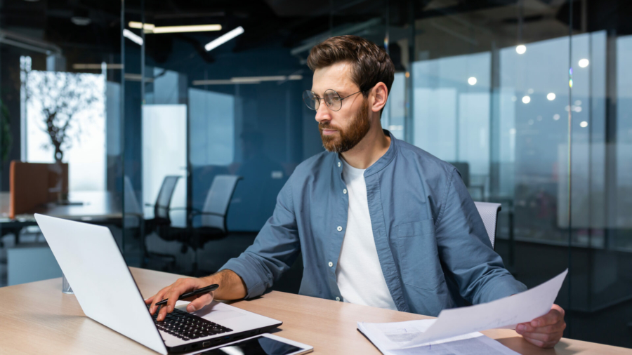 a-serious-young-man-accountant-financier-analyst-auditor-sits-in-the-office-at-the-table-he-holds-documents-and-a-pen-in-his-hands-checks-accounts-finances-types-on-a-laptop-stockpack-istock.jpg