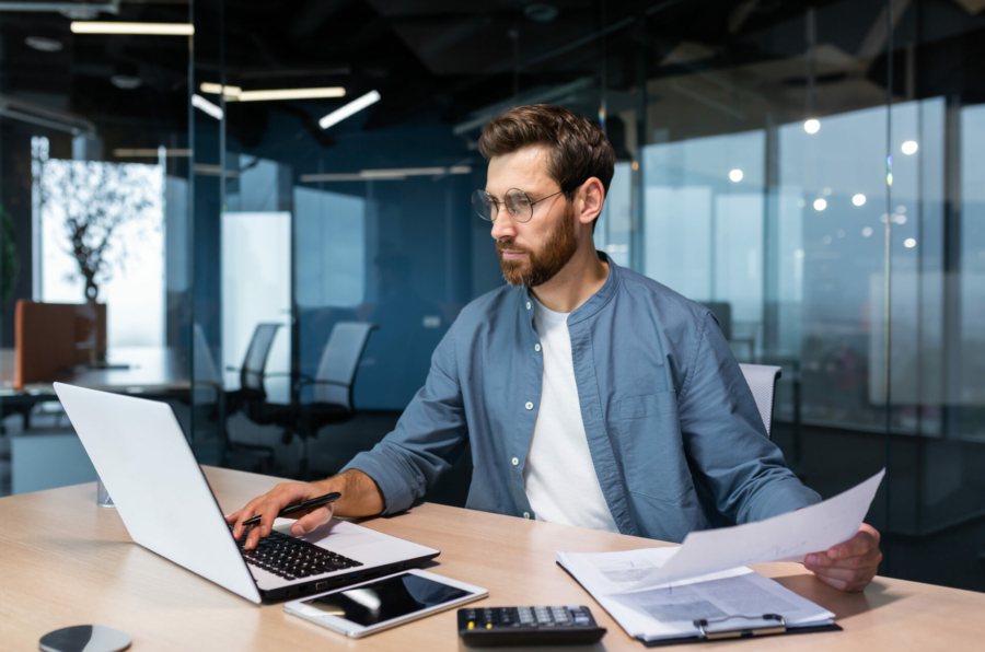 a-serious-young-man-accountant-financier-analyst-auditor-sits-in-the-office-at-the-table-he-holds-documents-and-a-pen-in-his-hands-checks-accounts-finances-types-on-a-laptop-stockpack-istock.jpg